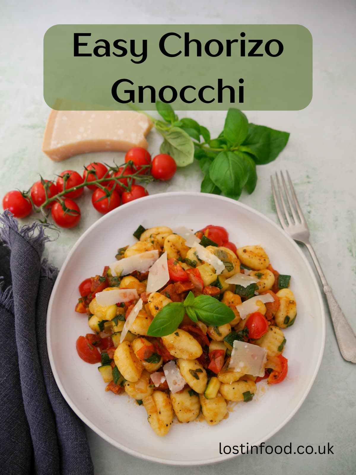 Pinnable image with recipe title and a white bowl filled with chorizo gnocchi with sauteed vegetables, garnished with fresh basil, with basil, tomatoes and parmesan cheese set alongside.