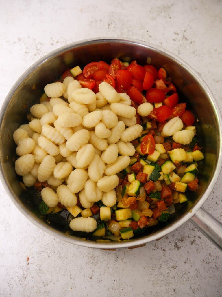 A large frying pan of sauteed chorizo and vegetables with cooked gnocchi.