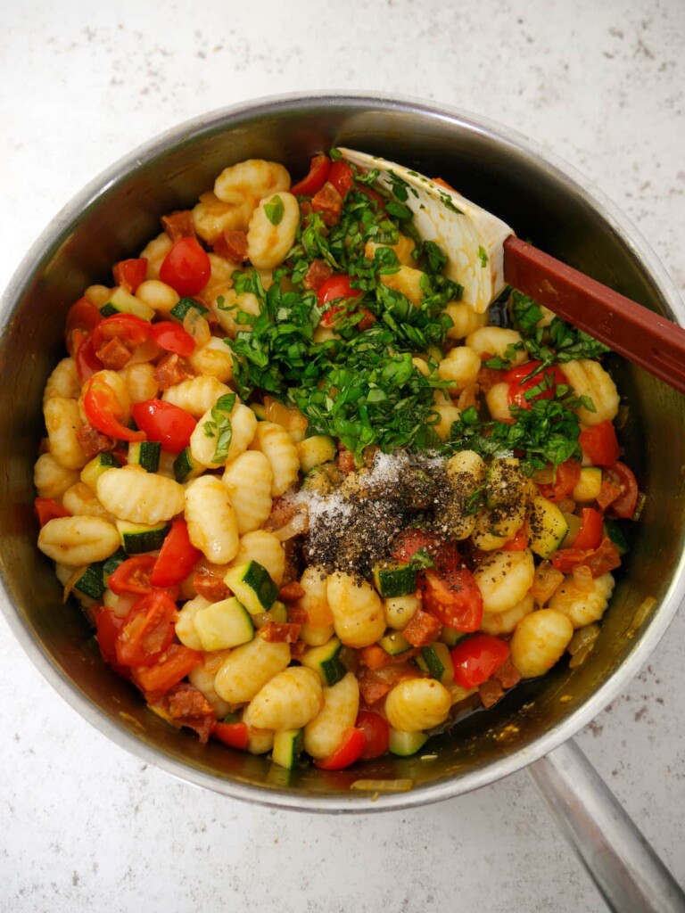 A large frying pan of sauteed chorizo and vegetables with cooked gnocchi, freshly chopped basil and seasoning.