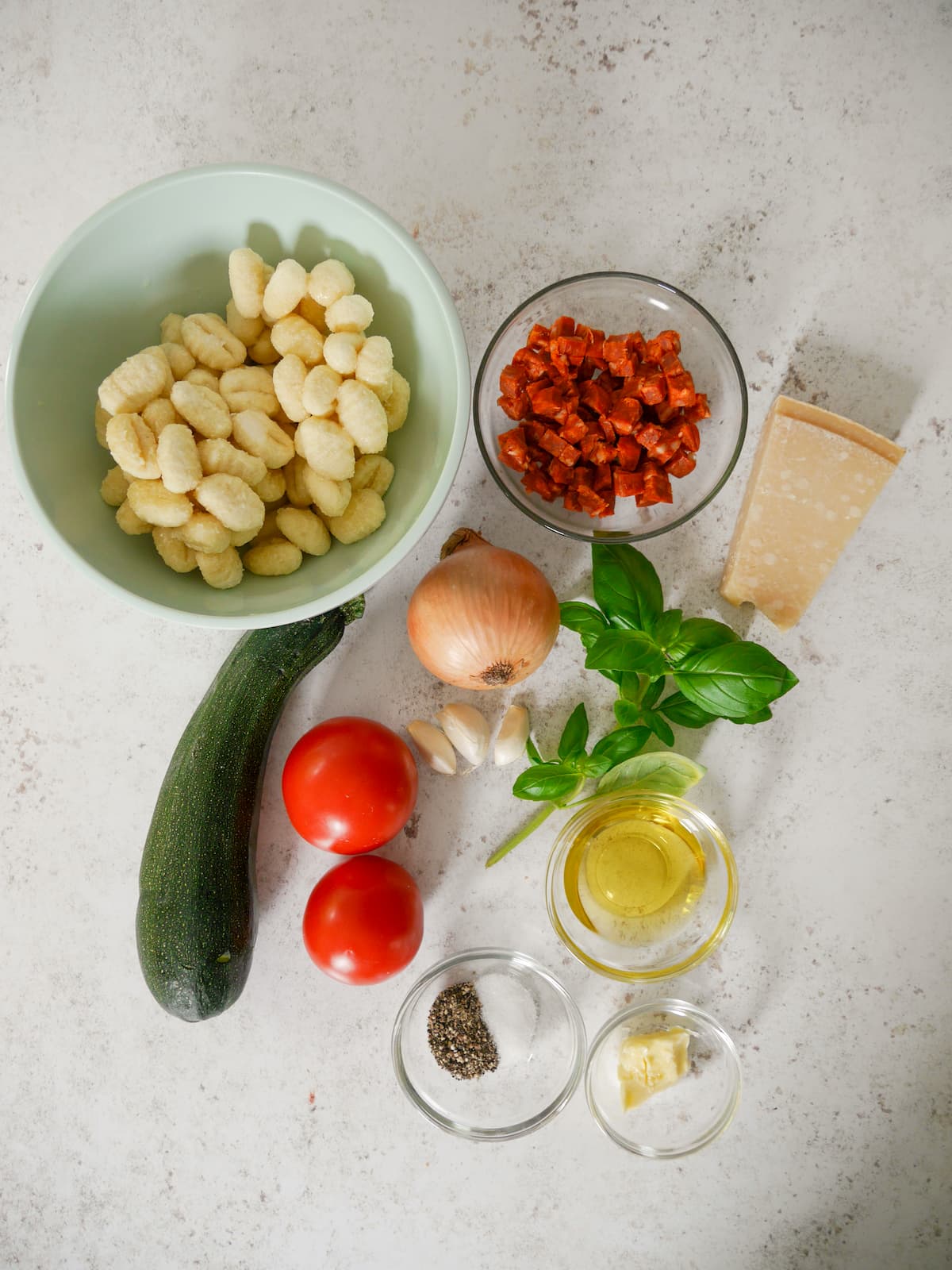 Individual recipe ingredients for chorizo gnocchi with courgette, onion, tomato, garlic and basil.