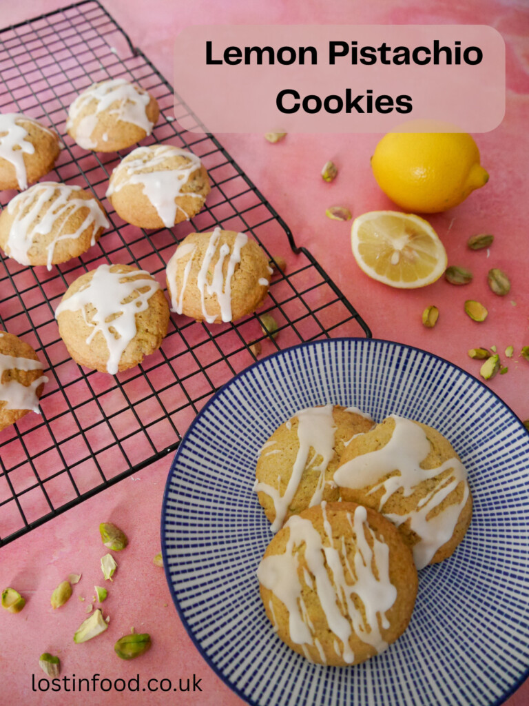 Pinnable image with recipe title and a stack of lemon pistachio cookies with a wire rack of cookies set alongside.