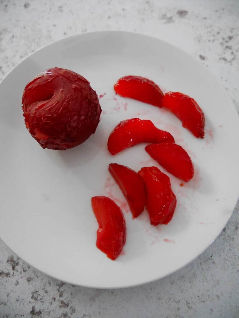 A plate topped with a whole mulled plum, with some wedged of mulled plum set alongside.