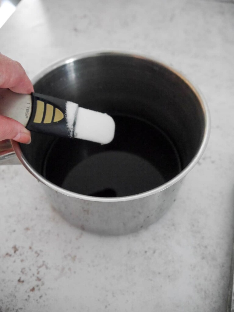 Caster sugar being added to mulled plum liquid.