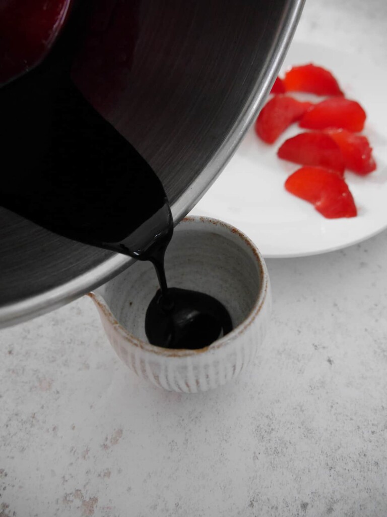 Mulled plum syrup being poured into a small jug.
