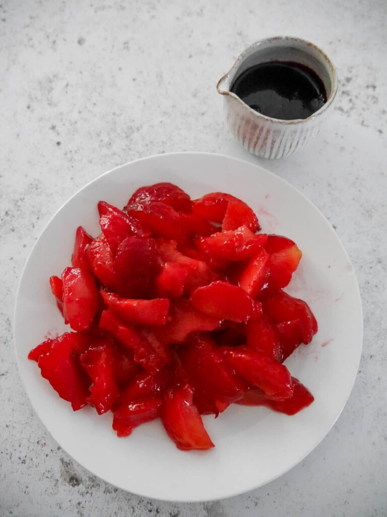 A plate of sliced mulled plums with a jug of mulled plum syrup set alongside.