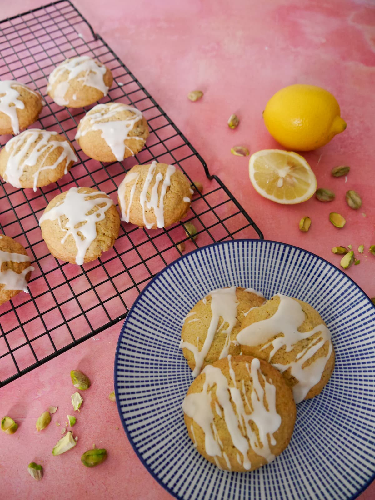 A blue and white plate topped with pistachio and lemon cookies, with more cookies set on a wire cooling rack set alongside.