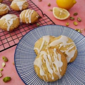 A blue and white plate topped with pistachio and lemon cookies, with more cookies set on a wire cooling rack set alongside.
