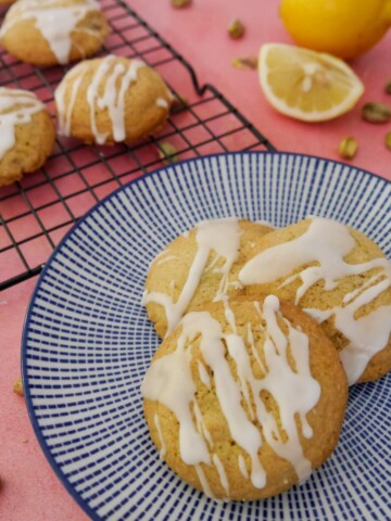 A blue and white plate topped with pistachio and lemon cookies, with more cookies set on a wire cooling rack set alongside.