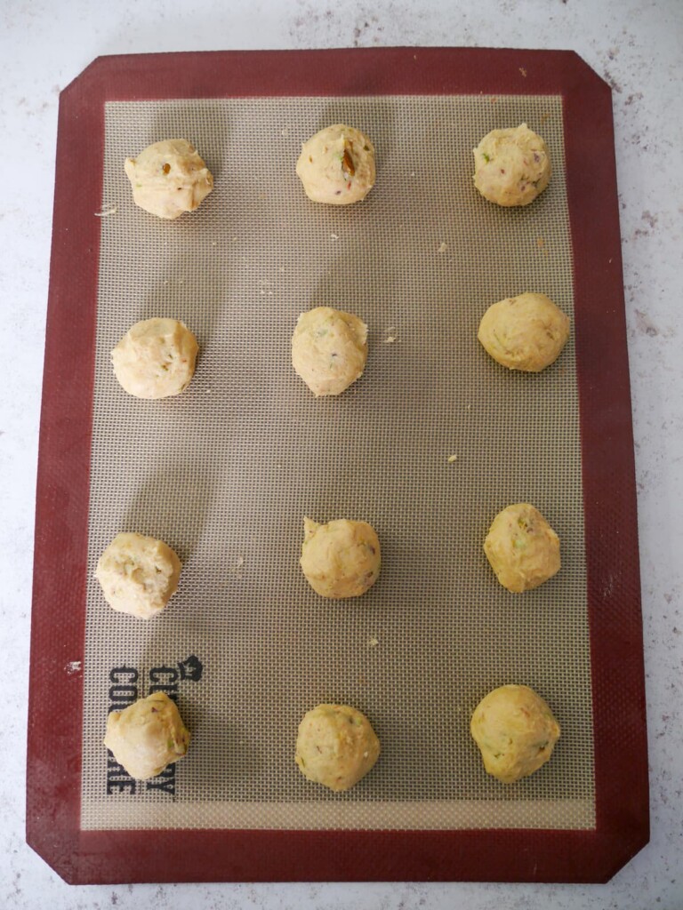 A baking sheet with a silicone liner topped with balls of pistachio and lemon cookie dough.