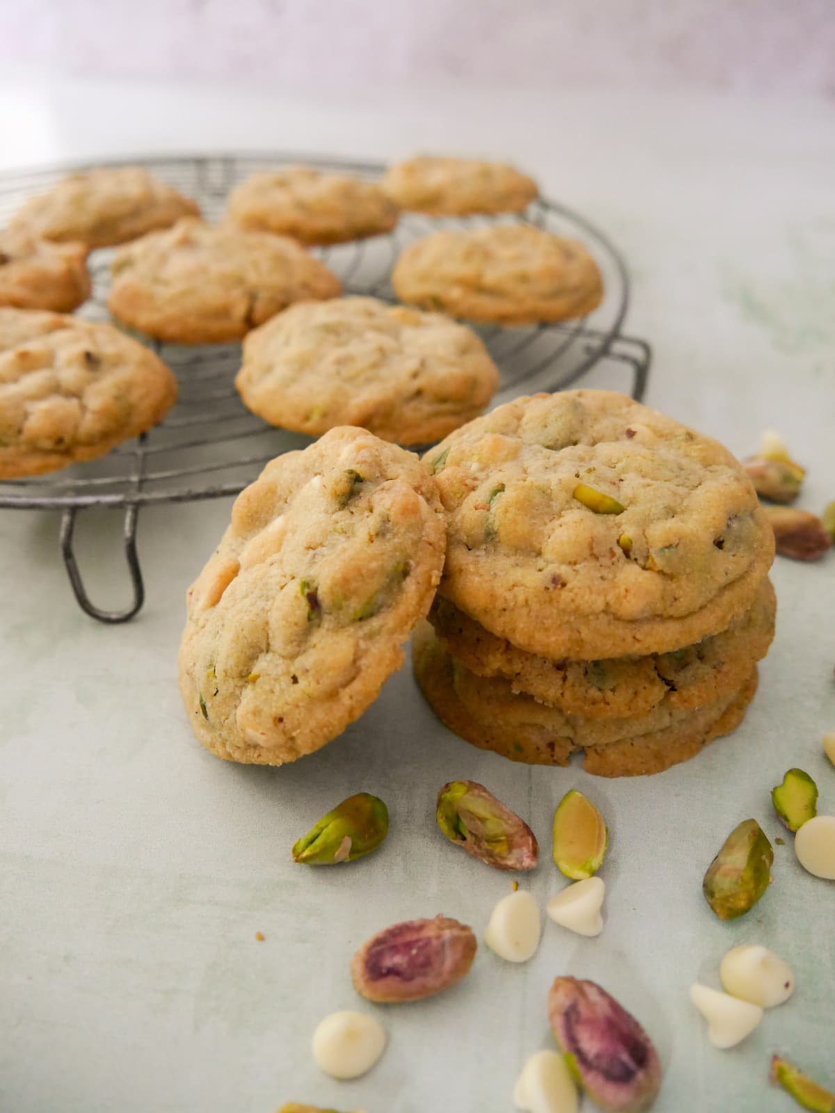 A stack of pistachio white chocolate cookies with a wire rack of cookies set alongside.