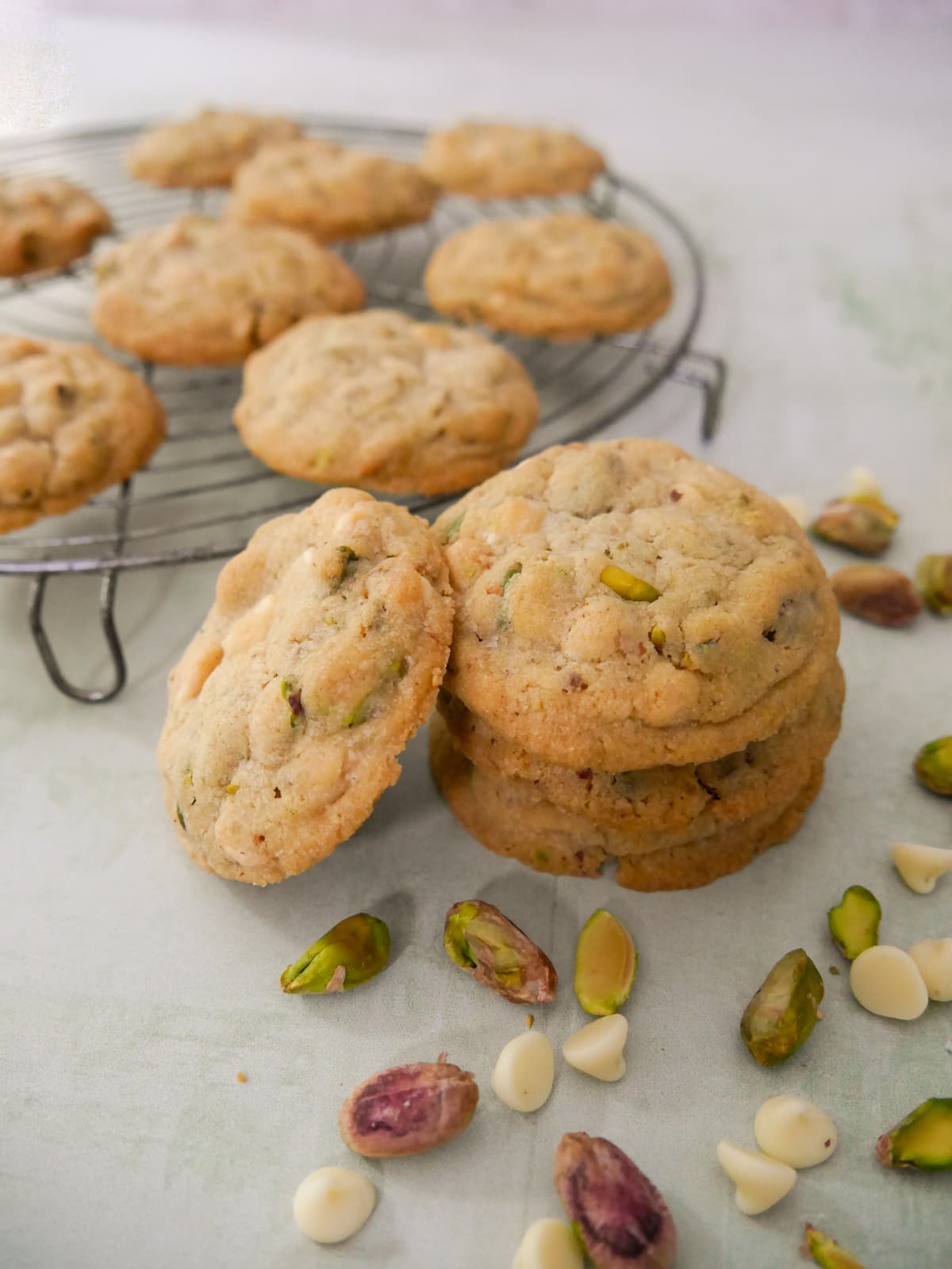 A stack of pistachio white chocolate cookies with a wire rack of cookies set alongside.