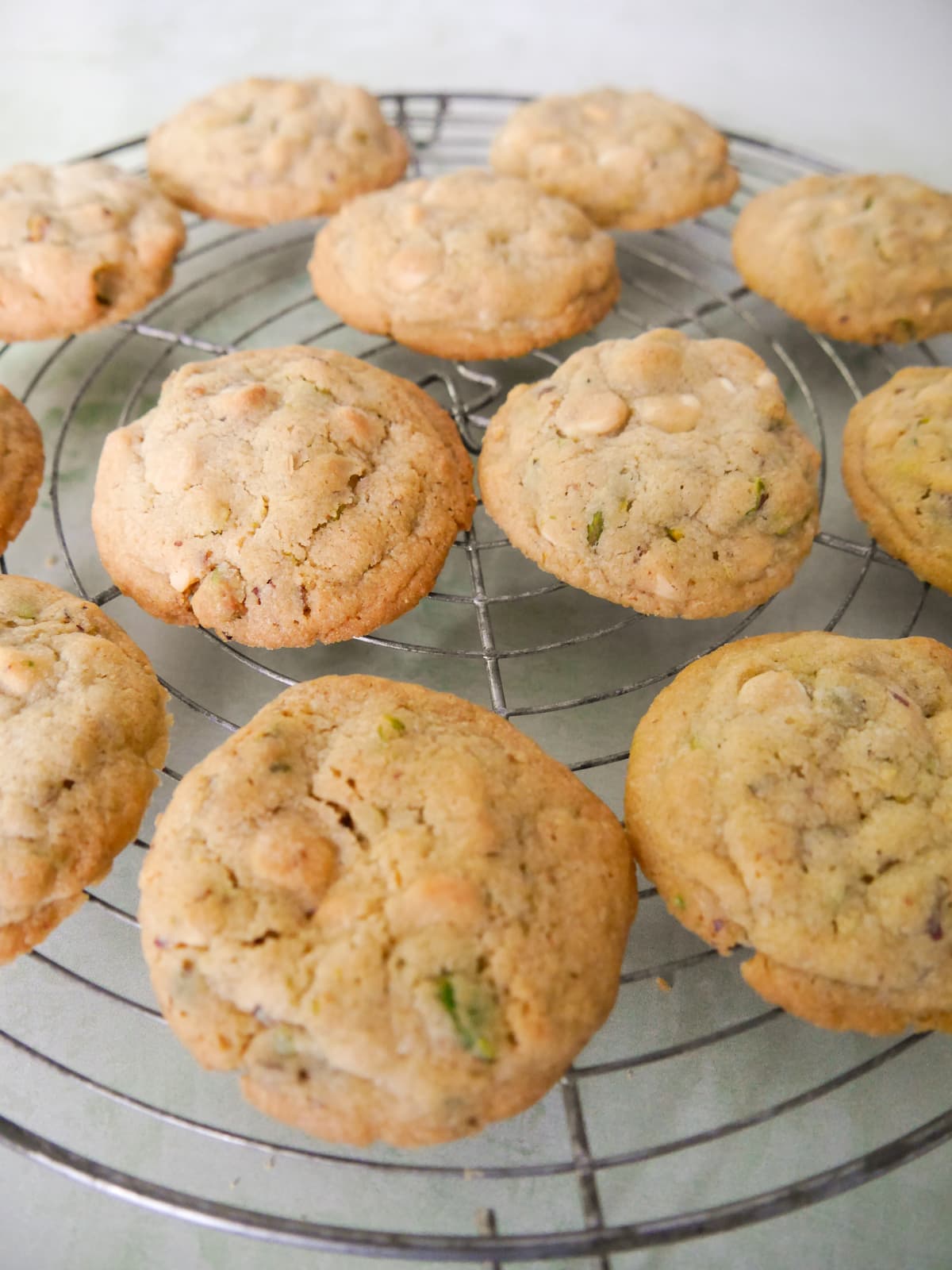 A wire cooling rack topped with pistachio white chocolate cookies.