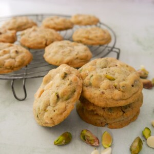 A stack of pistachio white chocolate cookies with a wire rack of cookies set alongside.