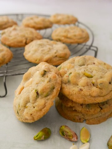 A stack of pistachio white chocolate cookies with a wire rack of cookies set alongside.