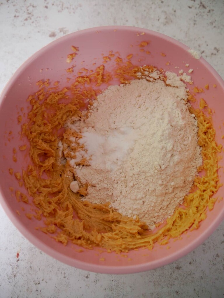 A bowl of creamed butter and sugar with added flour and baking powder.