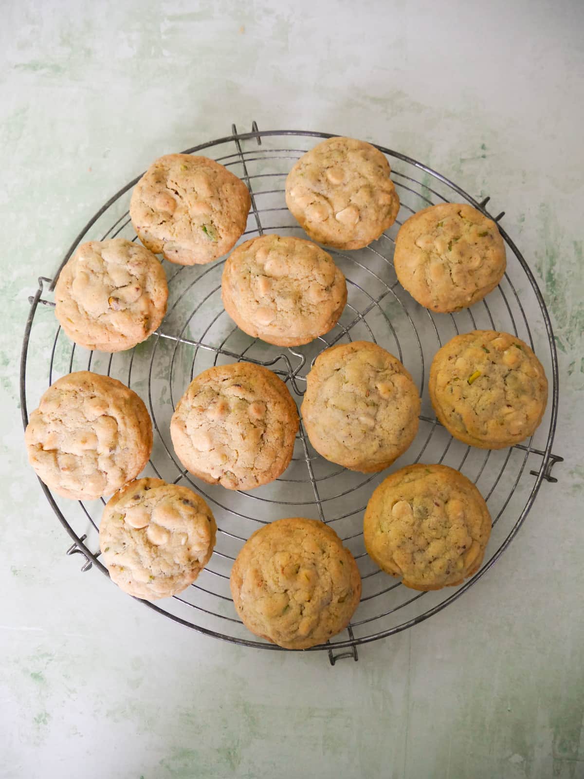 A wire cooling rack topped with pistachio and white chocolate cookies.