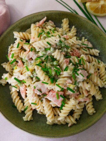 A green bowl filled with smoked salmon pasta garnished with chopped chives with a wedge of lemon and chives set alongside.