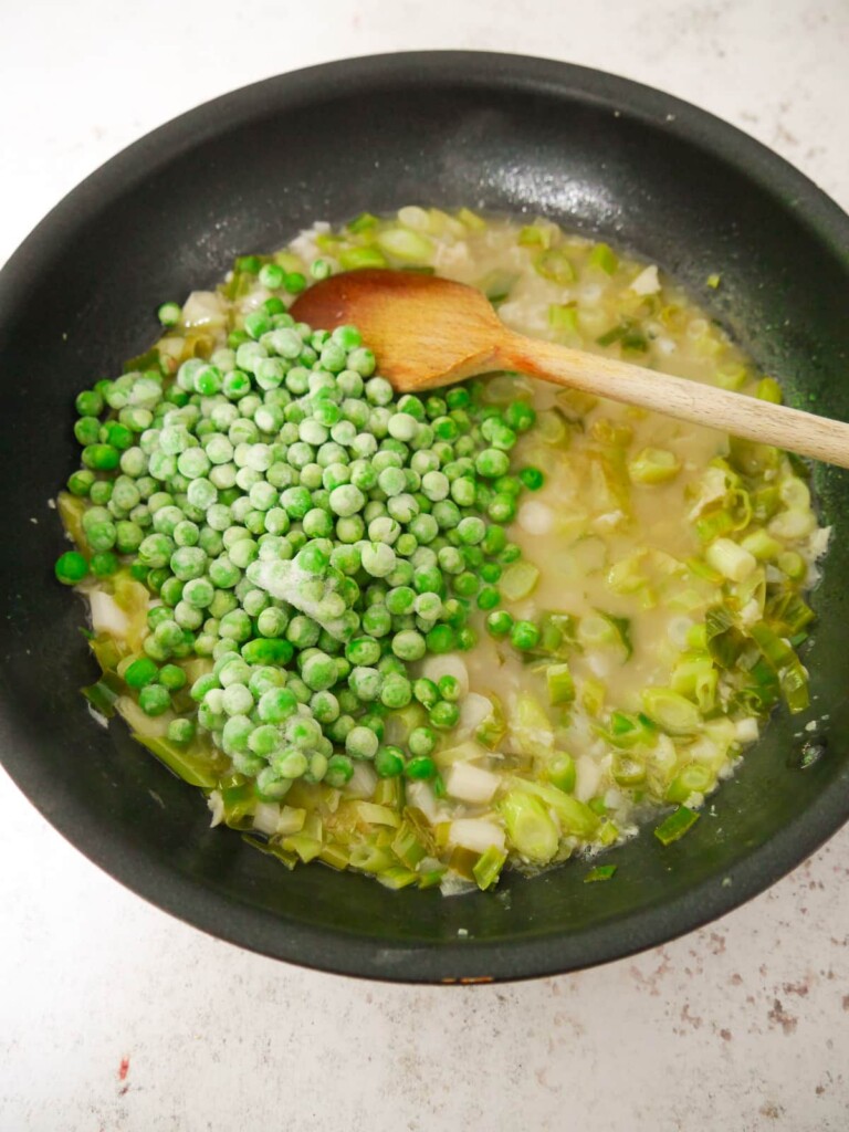 A large frying pan of sauteed vegetables and reduced white wine with added frozen garden peas.