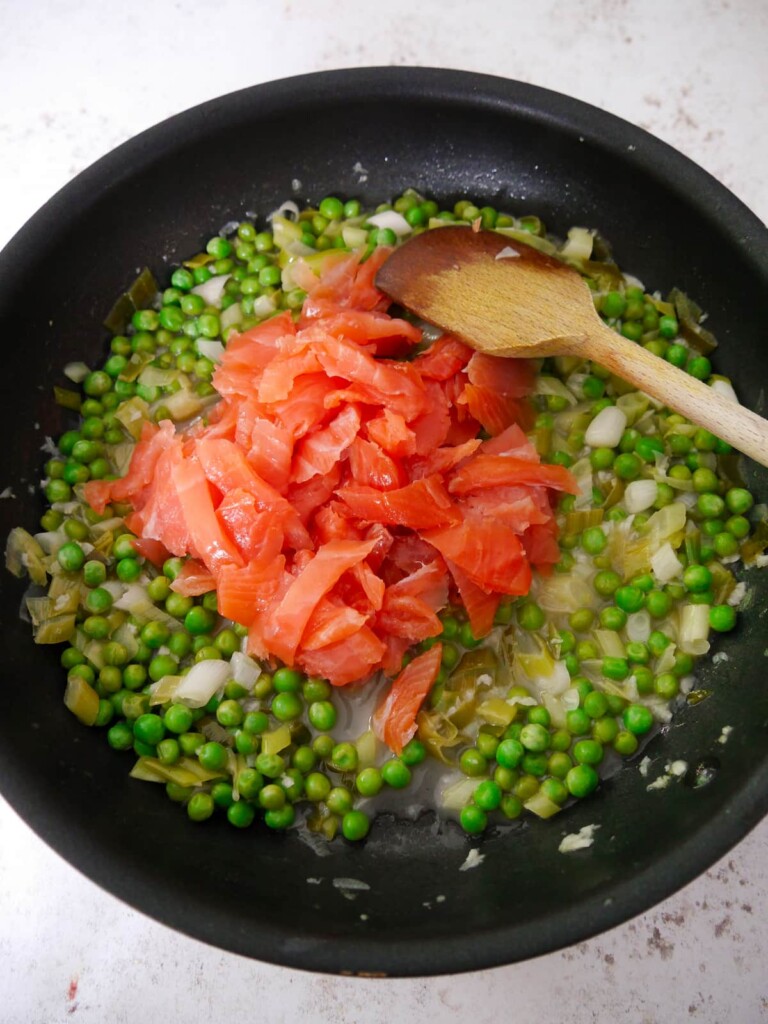 A large frying pan filled with sauteed vegetables in a reduced wine sauce with added smoked salmon.