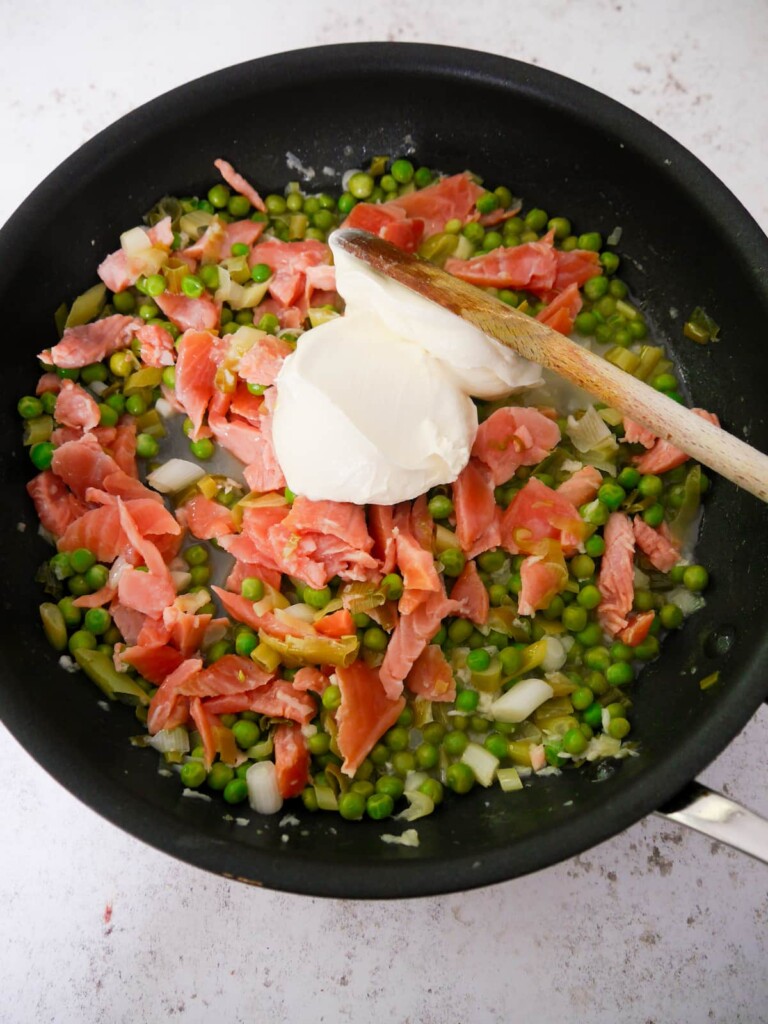A large frying pan filled with sauteed vegetables in a reduced wine sauce with added smoked salmon and creme fraiche.