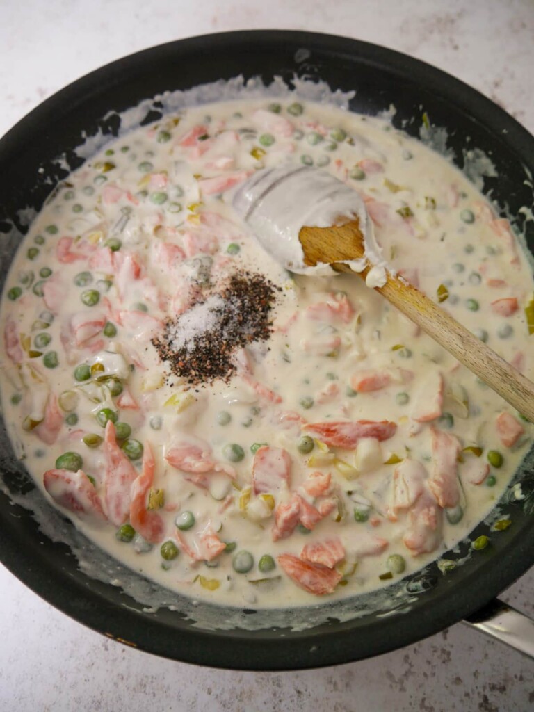 A large frying pan filled with a creamy smoked salmon pasta sauce, with garden peas, spring onions and seasoning.