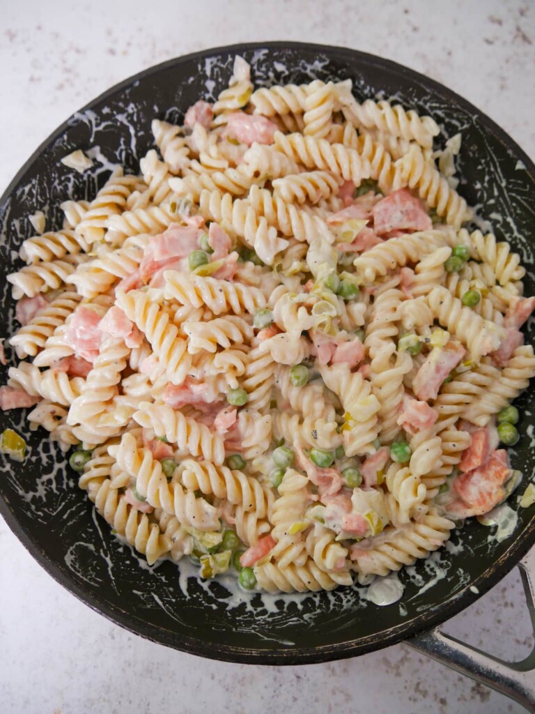 A large non stick pan filled with pasta in a creamy smoked salmon sauce.