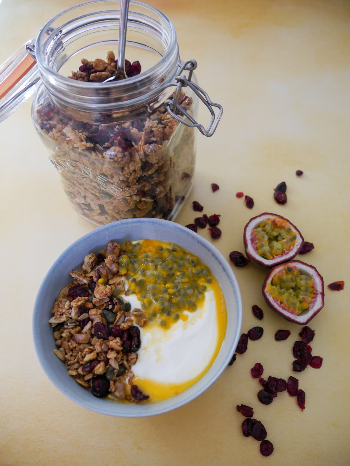 A bowl of Greek yogurt topped with spiced cranberry granola and passionfruit with a jar of granola set alongside.