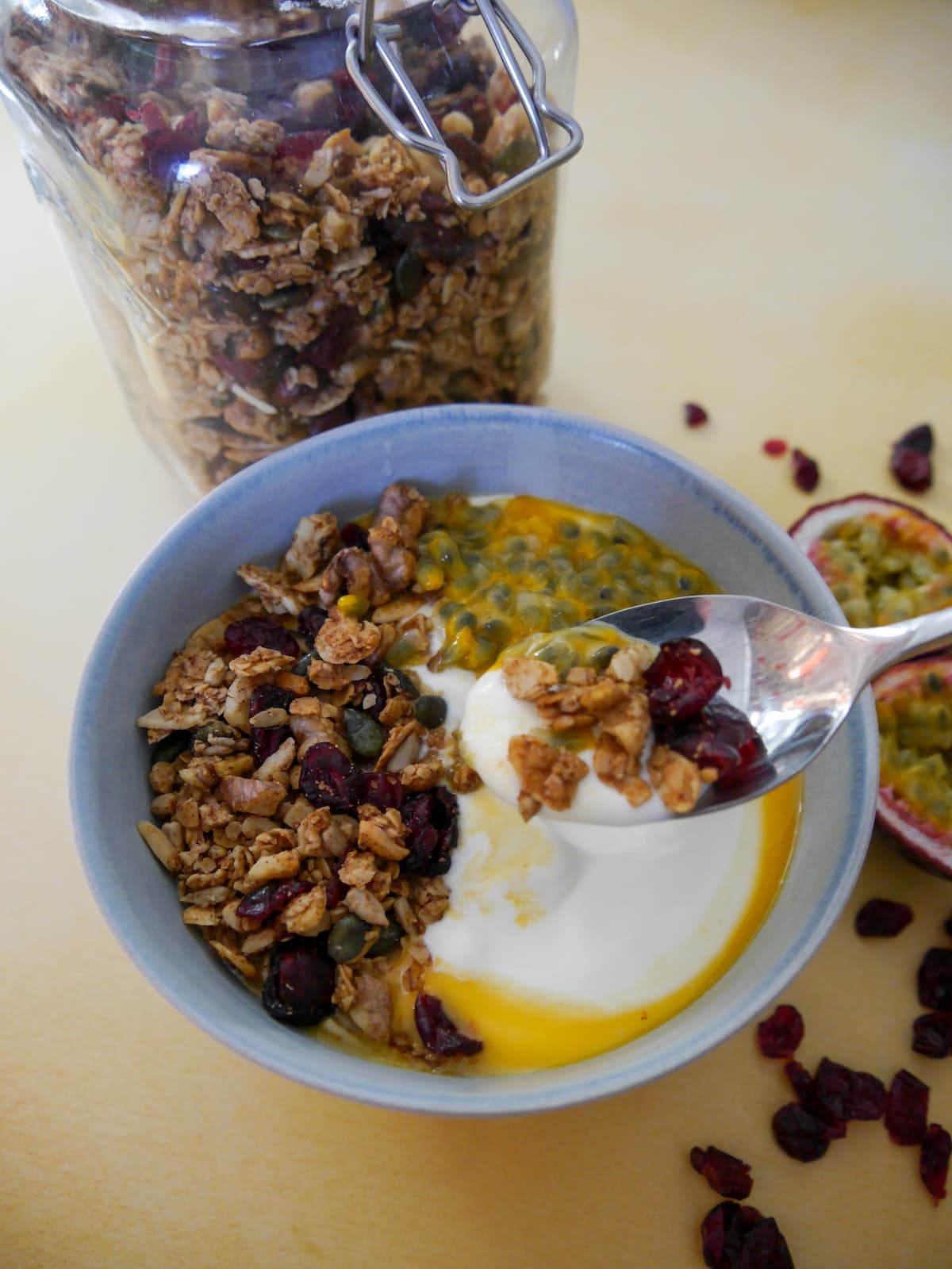 A bowl of Greek yogurt topped with spiced cranberry granola and passionfruit with a jar of granola set alongside.