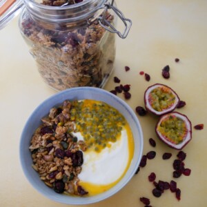 A bowl of Greek yogurt topped with spiced cranberry granola and passionfruit with a jar of granola set alongside.