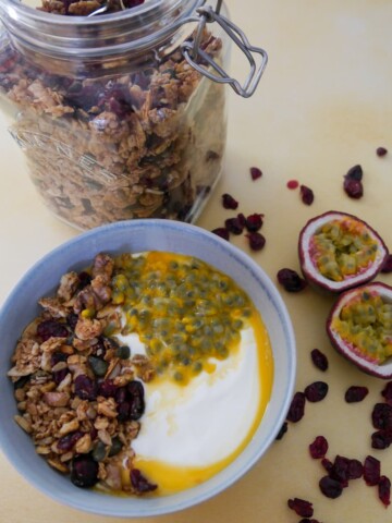 A bowl of Greek yogurt topped with spiced cranberry granola and passionfruit with a jar of granola set alongside.