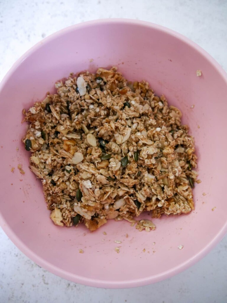 A bowl of dry granola ingredients with coconut oil and honey mixed through.