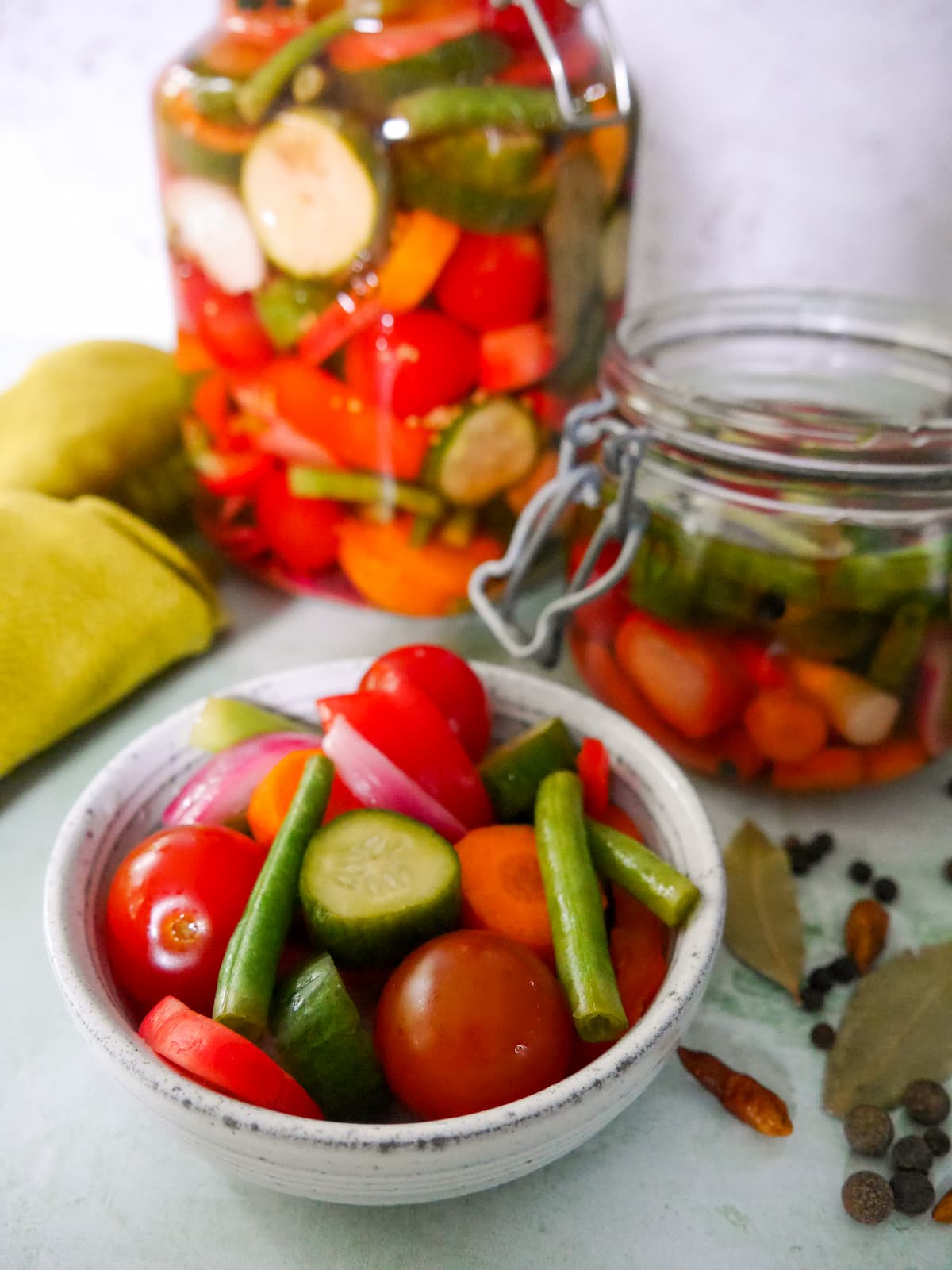 A bowl of summer pickled vegetables, with a large jar of pickled vegetables and some dry spices set alongside.