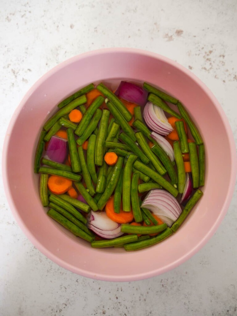 Green beans, sliced red onions and carrots in a bowl of heavily salted water.