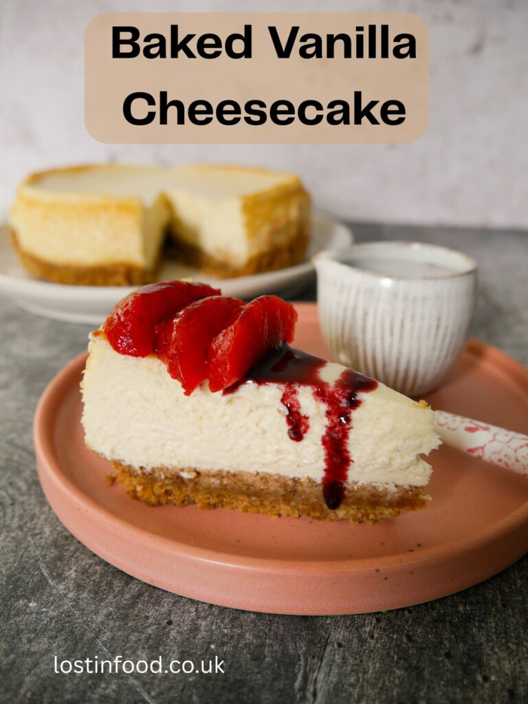 Pinnable image with recipe title and a plate with a slice of baked vanilla cheesecake, topped with some mulled plums and plum syrup, with the whole cheesecake set alongside.