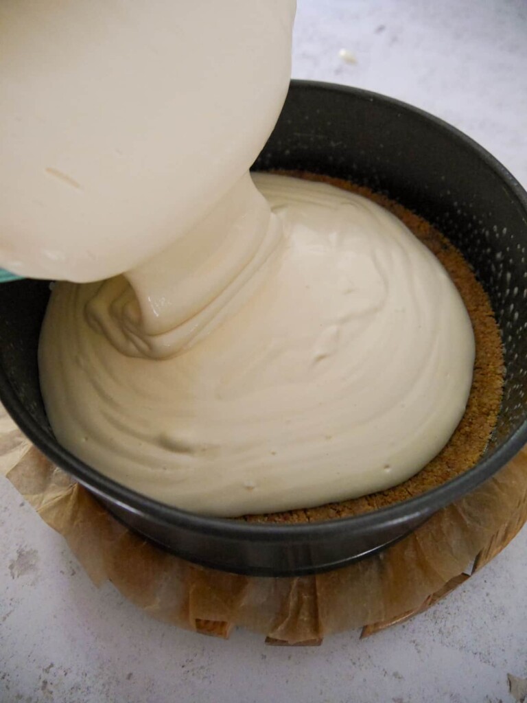 Vanilla cheesecake mixture being poured into a baking tin with a biscuit base.