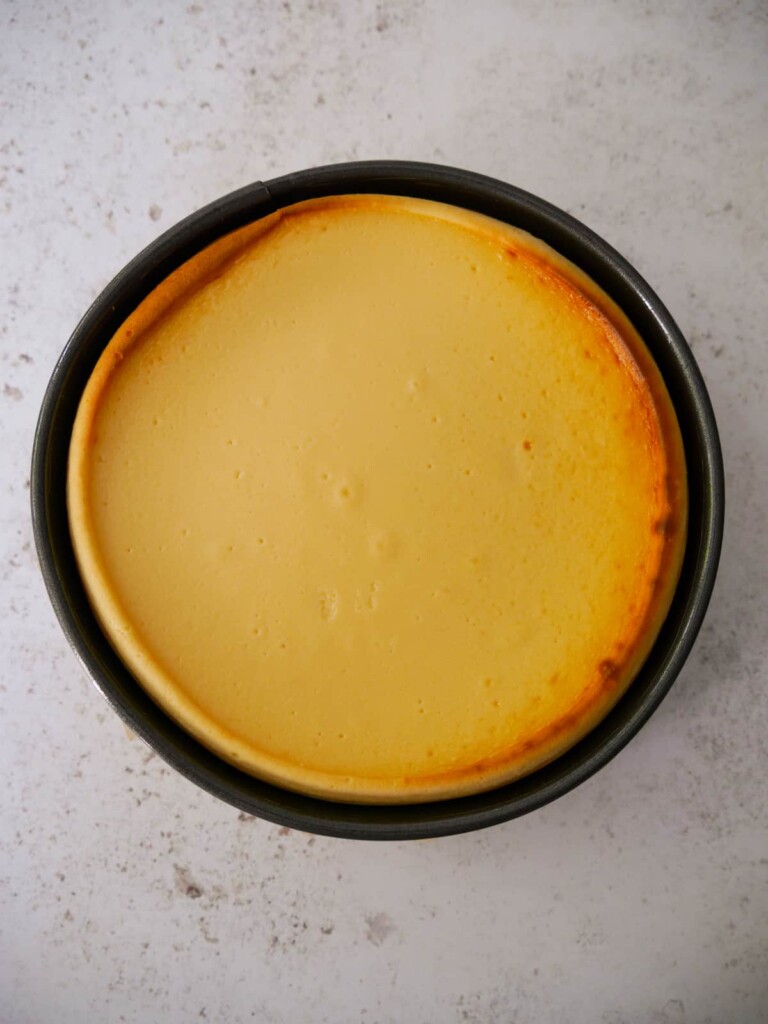 A baked vanilla cheesecake in the baking tin, set aside to cool.