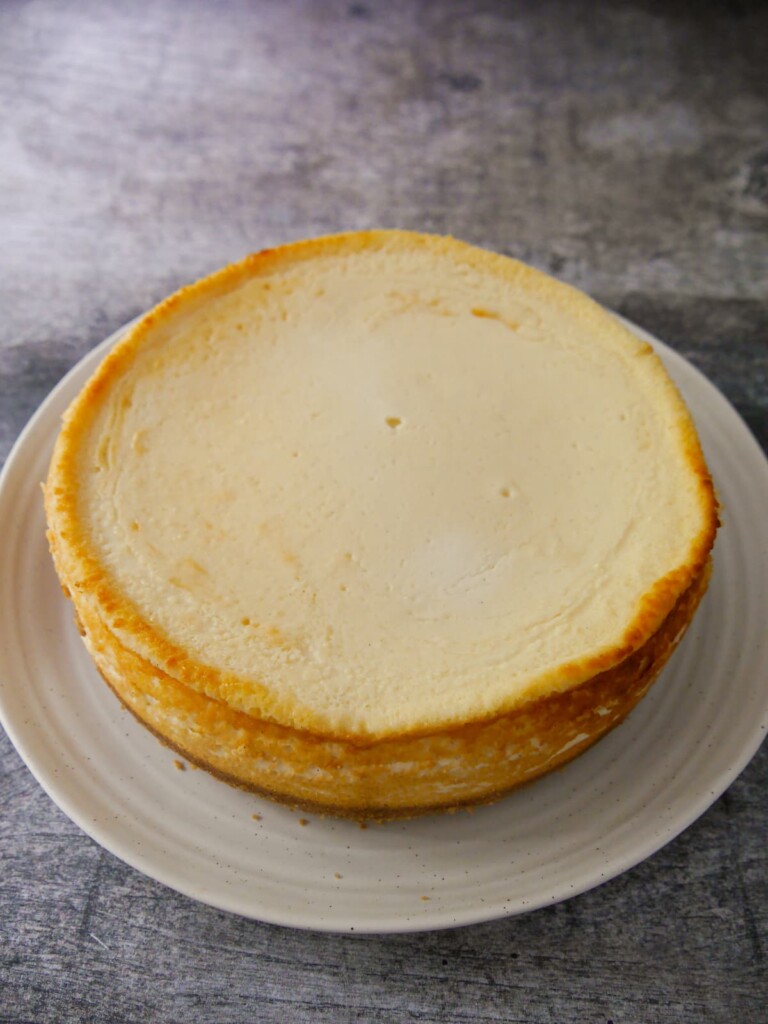A baked and chilled vanilla cheesecake removed from baking tin and set onto a plate.