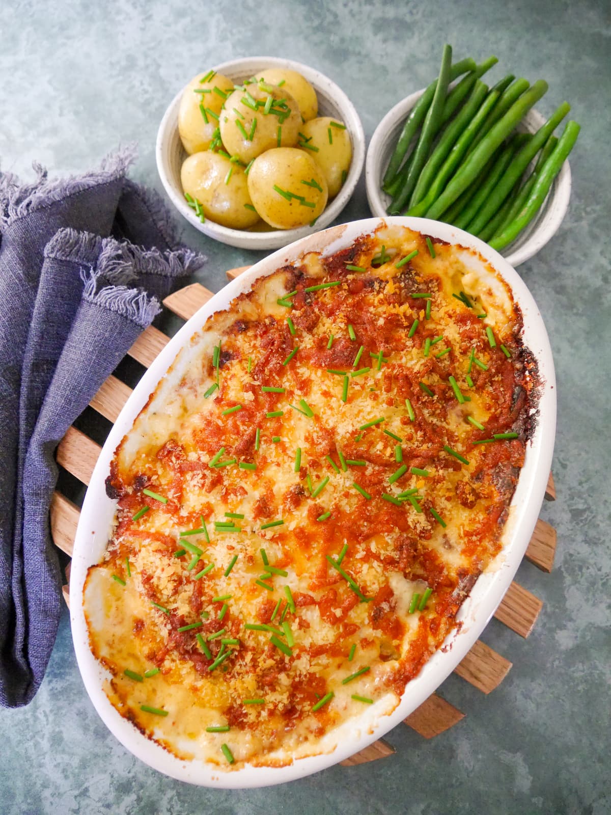 An oven proof dish of fish gratin served with sides of buttered chive new potatoes and green beans.