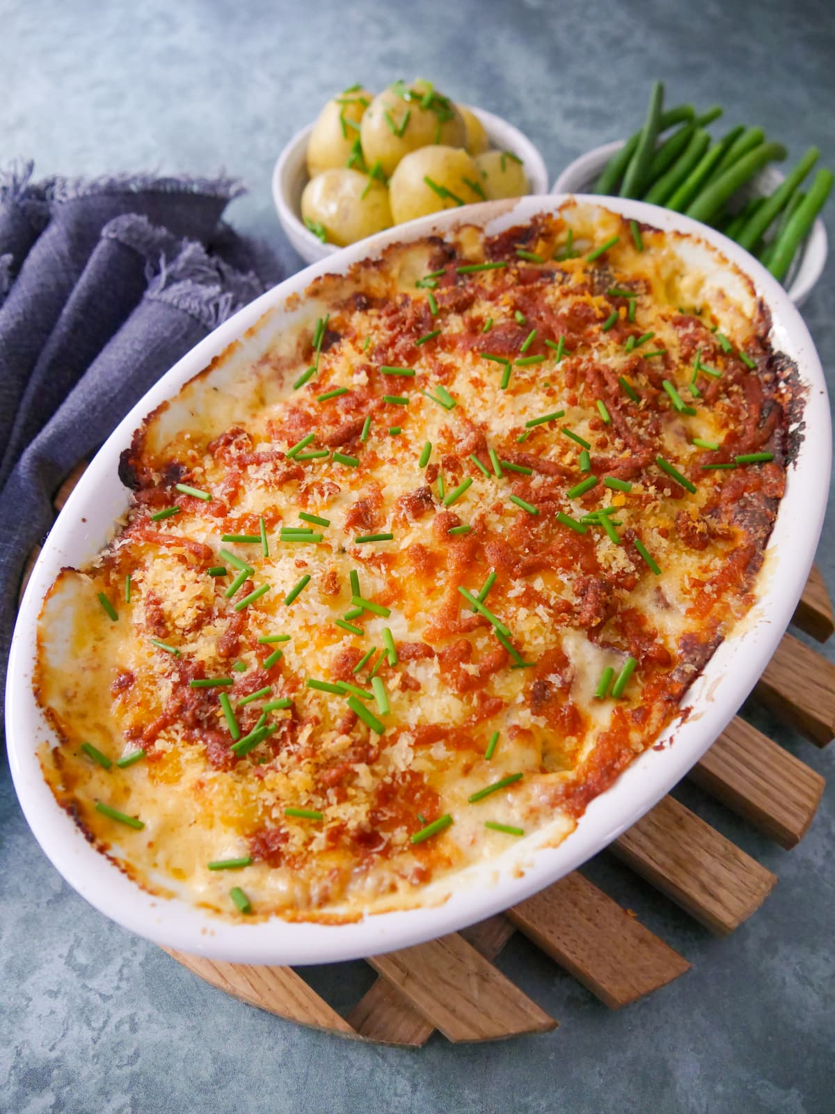 An oven proof dish of fish gratin served with sides of buttered chive new potatoes and green beans.