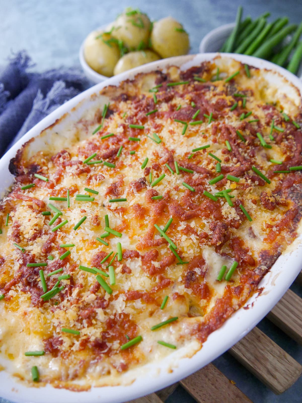 An oven proof dish of fish gratin served with sides of buttered chive new potatoes and green beans.