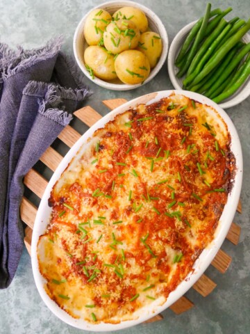 An oven proof dish of fish gratin served with sides of buttered chive new potatoes and green beans.