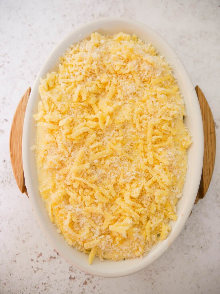 A white oven proof dish filled with cod fillets in a creamy sauce topped with cheese and breadcrumbs.