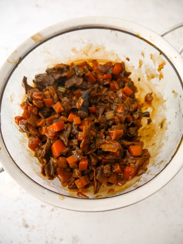 Vegan gravy and based vegetables being poured through a fine sieve.