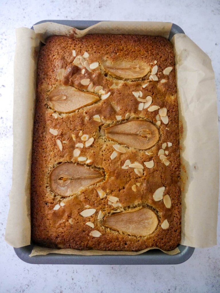 A paper lined baking tray filled with a baked pear and almond cake.