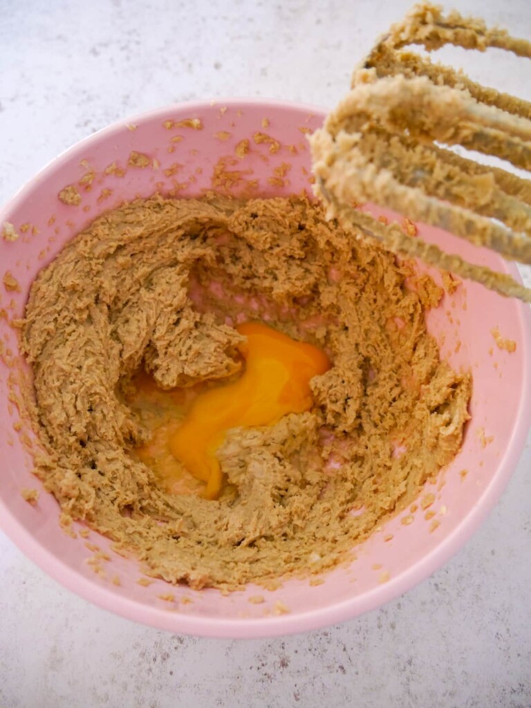 A pink bowl of beaten butter and sugar with added egg.