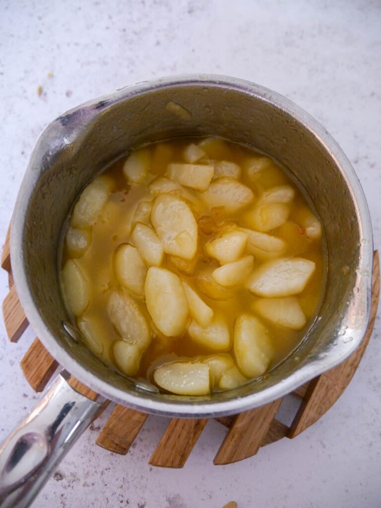 A saucepan of poached pear slices in a syrup.