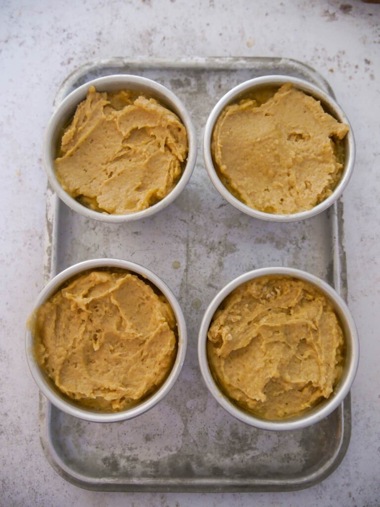 4 uncooked bowls of individual pear and ginger sponge puddings set on a baking tray.