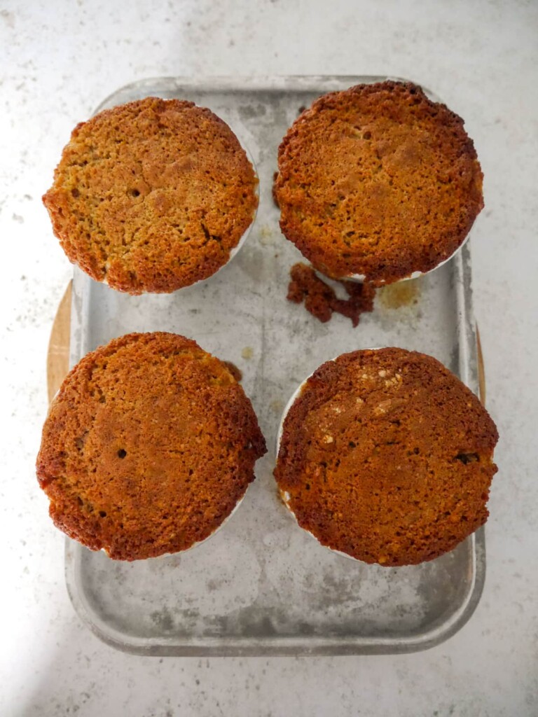 4 cooked bowls of individual pear and ginger sponge puddings set on a baking tray.