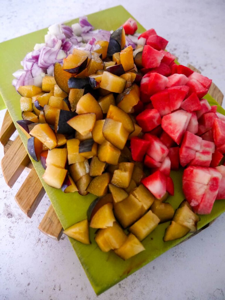 A board topped with chopped plums, apples and red onion.