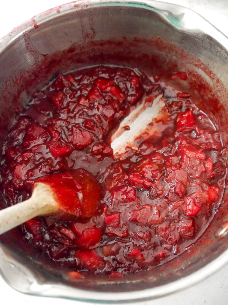A saucepan of cooked plum chutney with a wooden spoon being dragged through it to show it is cooked and ready to set.
